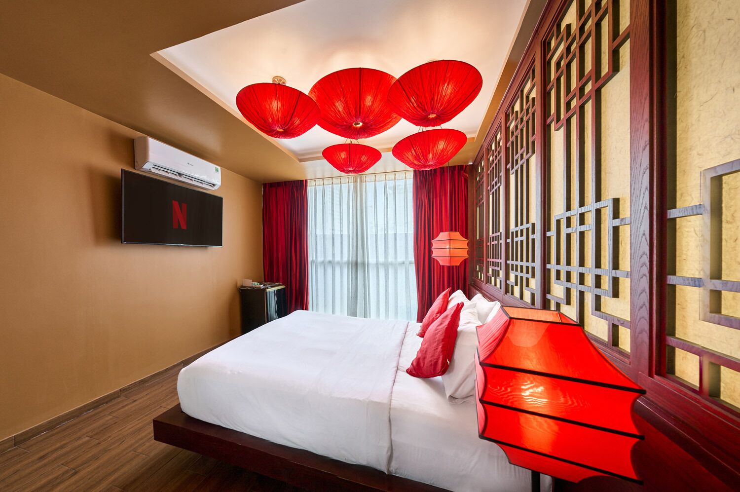 Une chambre d’hôtel avec un lit, un téléviseur fixé au mur et une fenêtre avec des rideaux rouges.