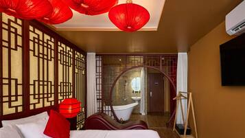 A hotel room with a bed, a red lantern, a round mirror, and a view of the bathroom.