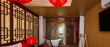 A hotel room with a bed, a red lantern, a round mirror, and a view of the bathroom.