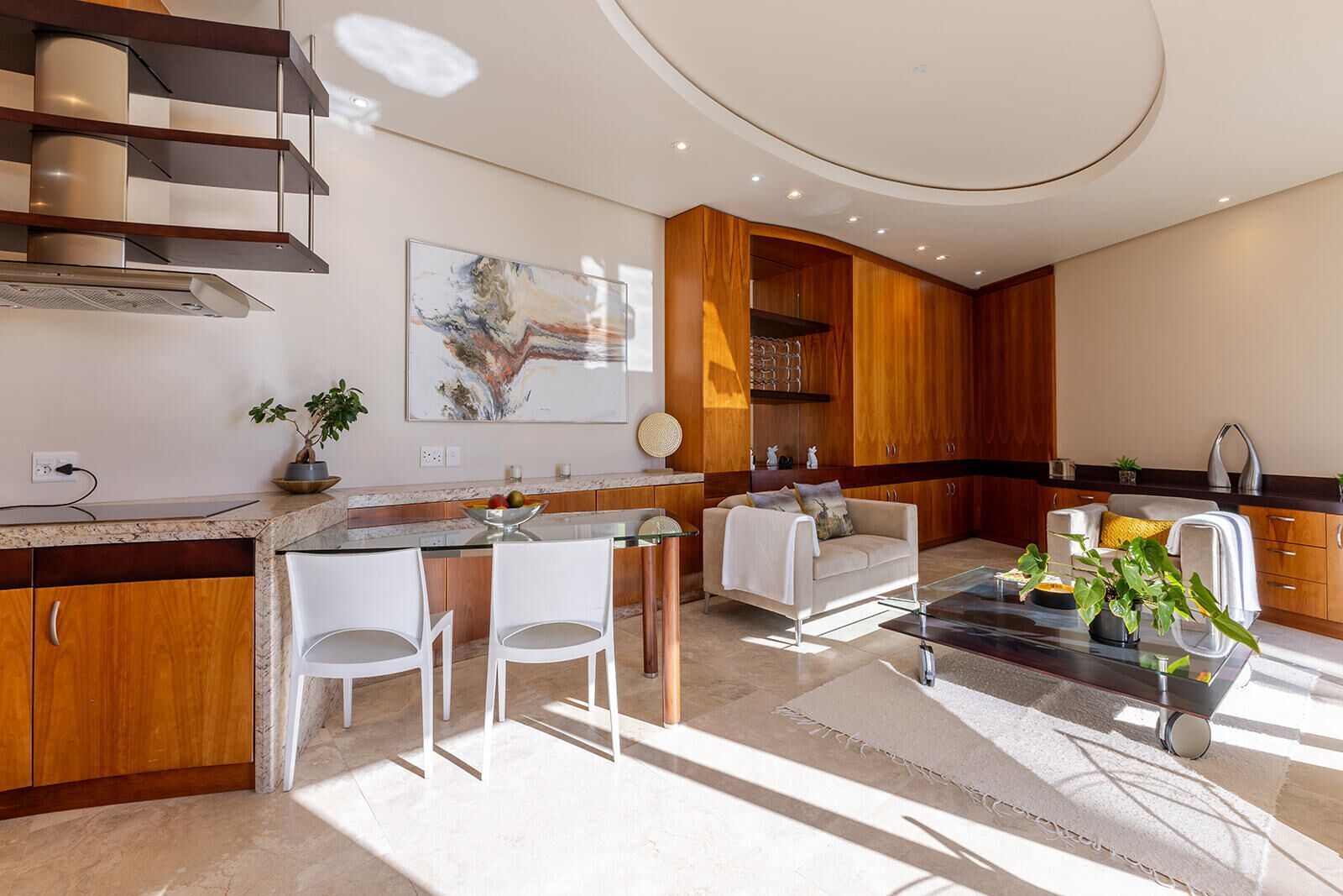 A modern kitchen with a dining area, featuring a kitchen island, white chairs, and a coffee table.