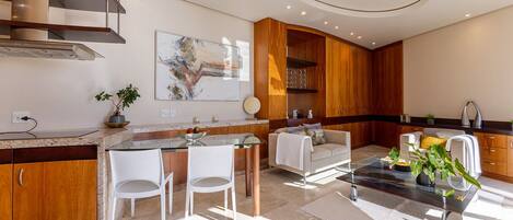 A modern kitchen with a dining area, featuring a kitchen island, white chairs, and a coffee table.