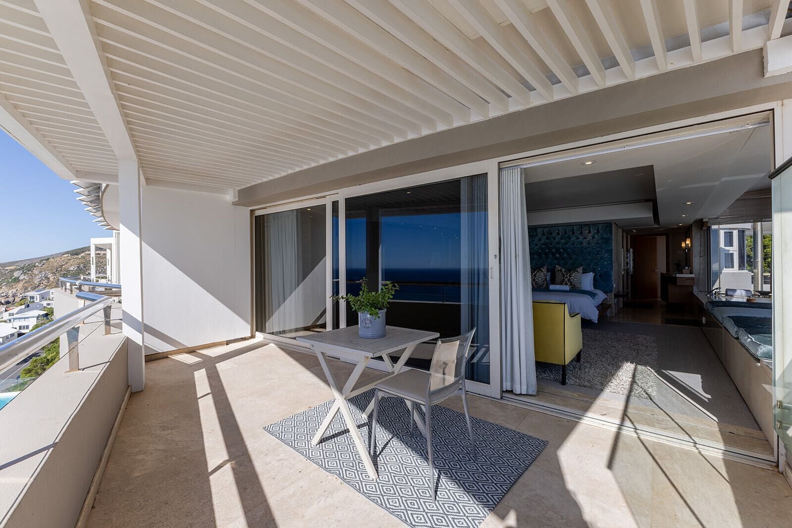 A balcony with a table and chairs, a potted plant, and a view of the sea.