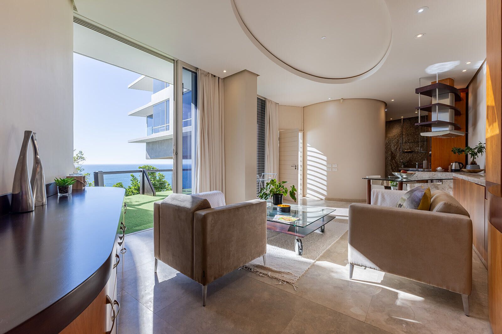 Een moderne woonkamer met een glazen salontafel, twee banken en uitzicht op de oceaan.