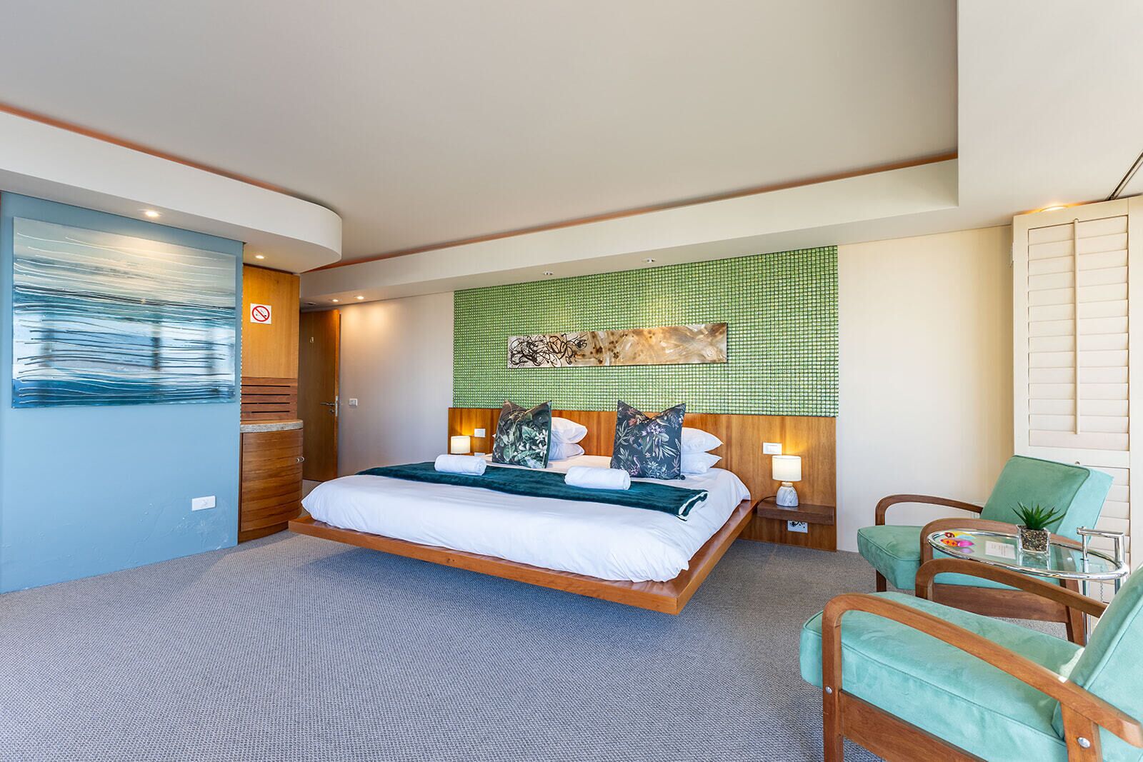 A modern hotel room with a large bed, a green wall, and a view of the city.