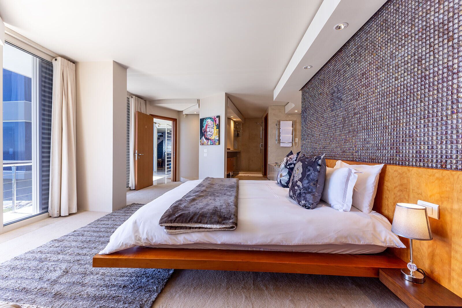 A modern hotel bedroom with a large bed, a view to the outside, and a unique textured wall.