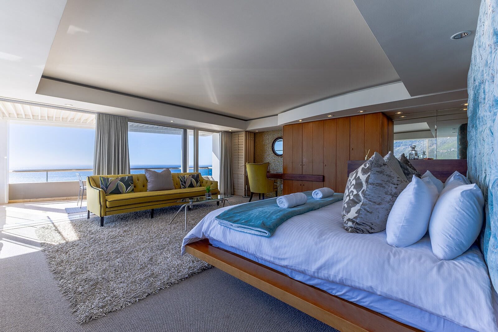 A modern bedroom with a large bed, a sofa, and a view of the sea.