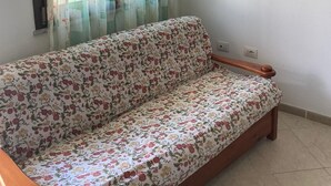 Ein Zimmer mit einer blumigen Couch, einem roten abstrakten Gemälde an der Wand und einem Fenster mit transparenten Vorhängen.