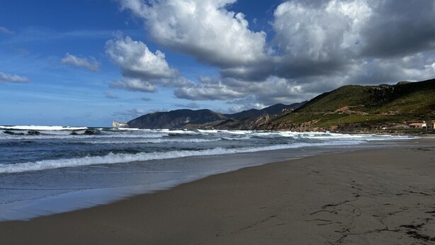 Ein Strand mit Wellen, blauem Himmel und Bergen in der Ferne.