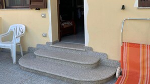 Ein Gebäudeeingang mit einer Treppe, die zu einer Tür führt, einem weißen Kunststoffstuhl und einem gestreiften Stoffteil am Boden.