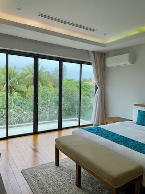 Relax on the balcony with a view of lush greenery and palm trees, featuring a large bed and a comfortable seating area.