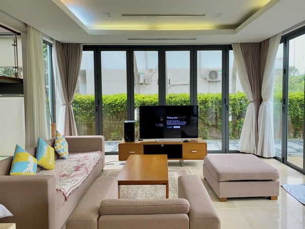 Relax in this stylish living room with a flat-screen TV, comfortable sofas, and a balcony offering views of lush greenery.