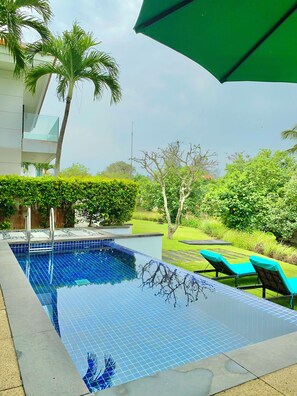 Relax by the clear blue pool surrounded by lush greenery and a modern building with a glass balcony.