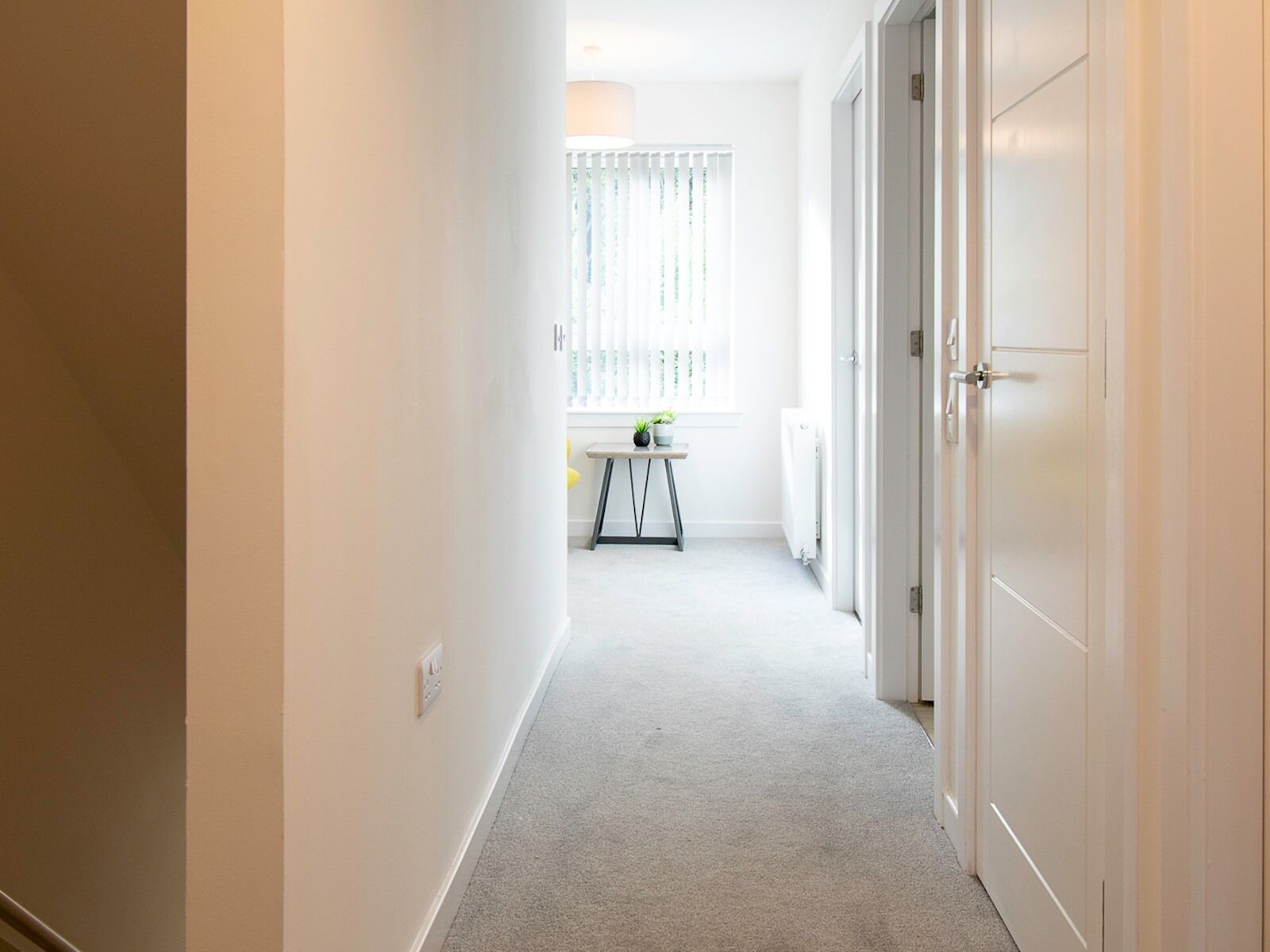A narrow hallway with a carpeted floor, white walls, and a door on the right.