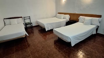 Une chambre d’hôtel avec trois lits simples, une chaise et une petite table.