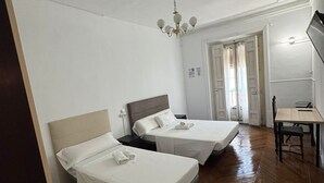 Een hotelkamer met twee bedden, een houten vloer, een bureau met stoel en een kroonluchter.