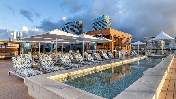 A rooftop pool with lounge chairs and umbrellas, surrounded by modern buildings and a clear sky. - HGVC Hokulani Waikiki Luxury, 1 BR Suites, Rooftop Pool/Spa, Close to Ft Derussy (Honolulu)