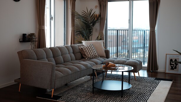A modern living room with a grey sofa, a round coffee table, and a large window with curtains. - ベッド3台でグループ滞在も快適！ウォーターサーバー付きの暮らせる民泊です (沖縄市)