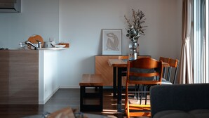 A modern living room with a ceiling fan, a dining area with a wooden table and chairs, and a kitchen area with a sink and countertop. - ベッド3台でグループ滞在も快適！ウォーターサーバ  ー付きの暮らせる民泊です (沖縄市)