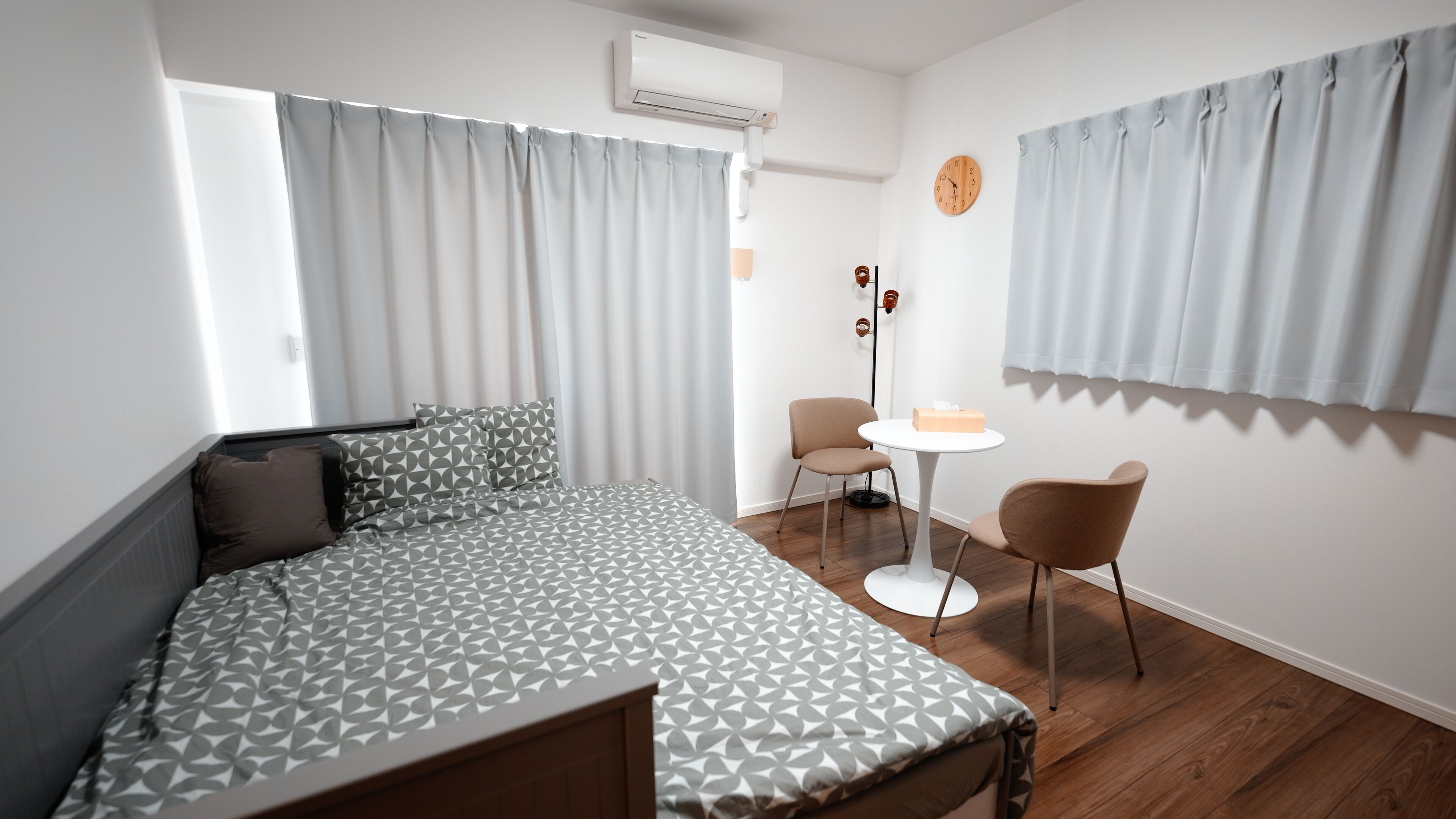 Een moderne slaapkamer met een bed, een klein tafeltje, twee stoelen en een airconditioning.