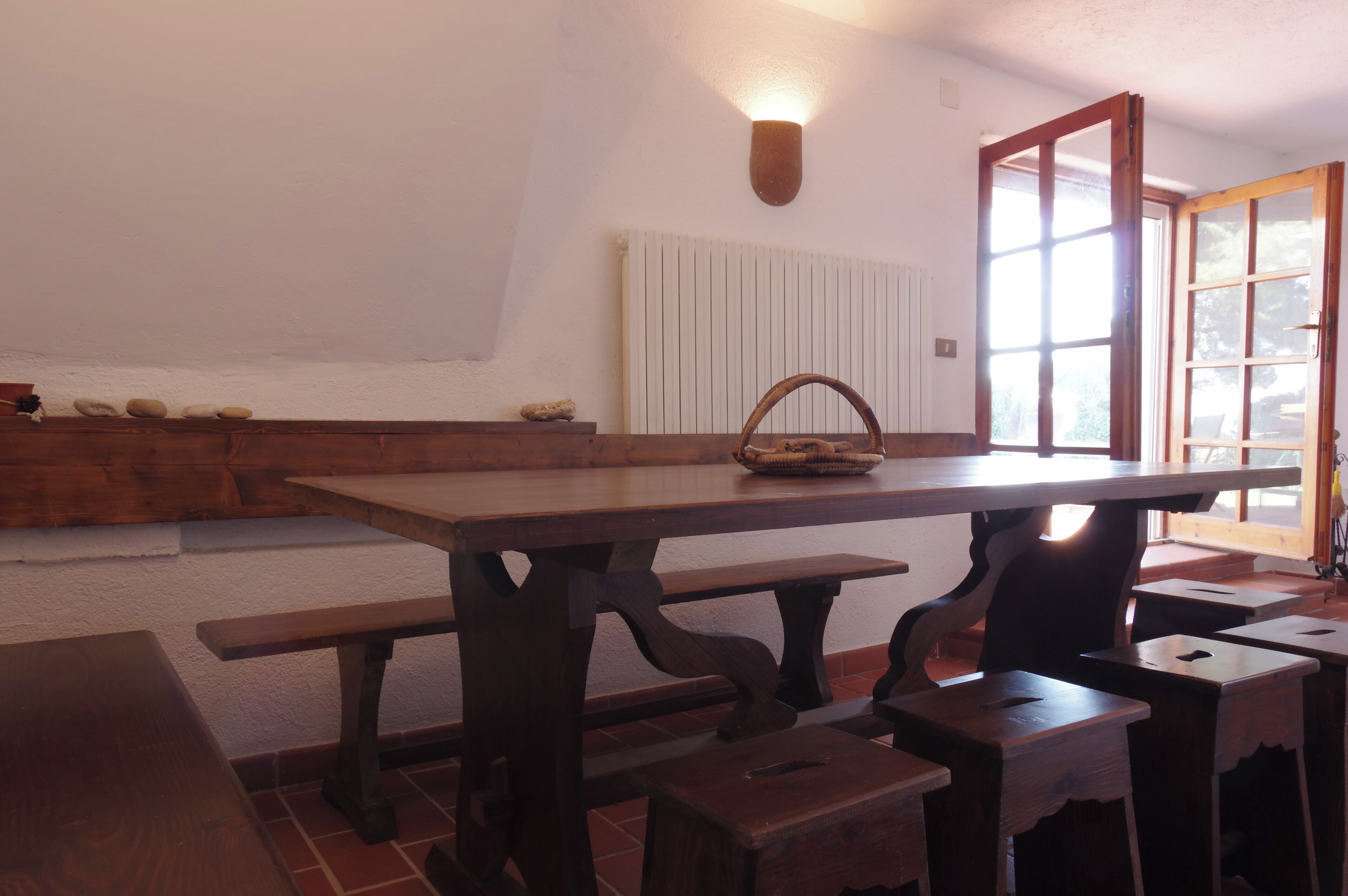 Una mesa de madera con bancos, una cesta y una ventana que da al exterior.