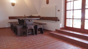 A dining area with a long wooden table and benches, a radiator, and a window with a view.