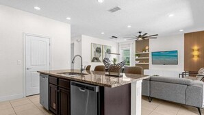 A modern kitchen with a built-in dishwasher, a granite countertop, and a dining area with a gray sofa and a ceiling fan. - Last Minute Disney! Private Pool, Hot Tub, Game Room & Themed Bedrooms. Book Now! #20220 (Orlando)