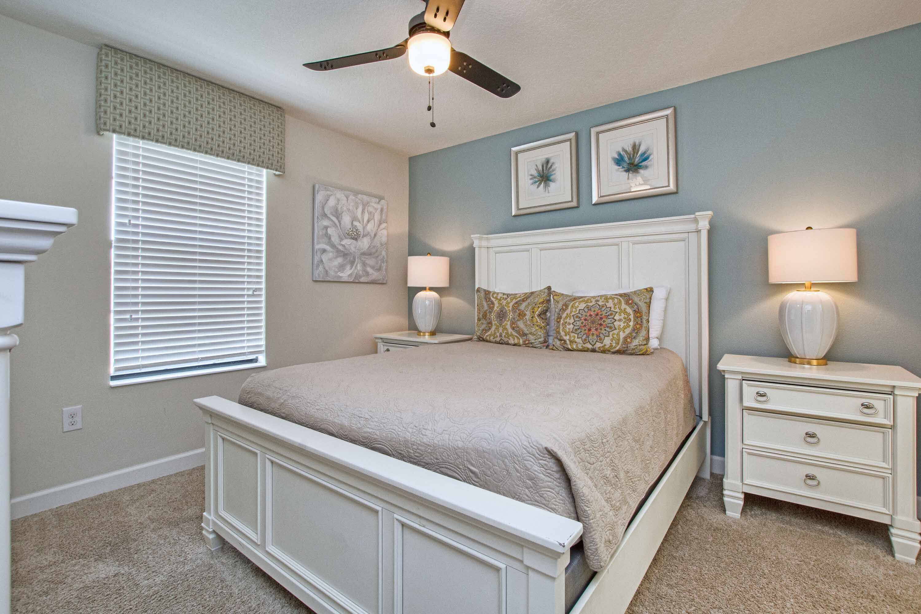 A bedroom with a bed, nightstands, a ceiling fan, and artwork on the walls.