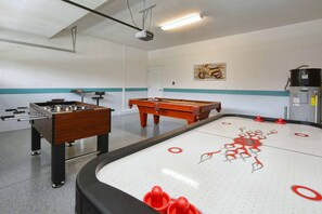 Een kamer met een tafelvoetbaltafel, pooltafel en een projector aan het plafond.