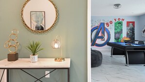 A room with a marble table, a potted plant, a lamp, and a wall with comic book art. - Last Minute Disney! Private Pool, Hot Tub, Game Room & Themed Bedrooms. Book Now! #38250 (Orlando)
