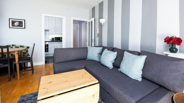 A modern living room with a grey sectional sofa, a wooden coffee table, and a dining area with a table and chairs. - Chic 2Bed W/Canal Views, 15 Min to Kilmainham Gaol (Kilmainham)