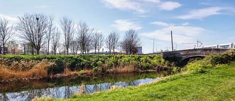 A stone bridge over a calm river, surrounded by lush greenery and leafless trees.