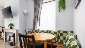 A cozy living room with a round wooden table, a sofa with checkered cushions, a fireplace, a TV mounted on the wall, and a hanging plant. - Chic 2Bed W/Canal Views, 15 Min to Kilmainham Gaol (Kilmainham)