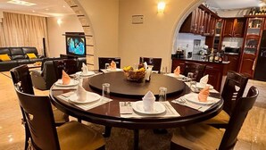 Una mesa redonda para seis personas, con sillas de madera oscura, una cesta de frutas en el centro y un televisor al fondo.