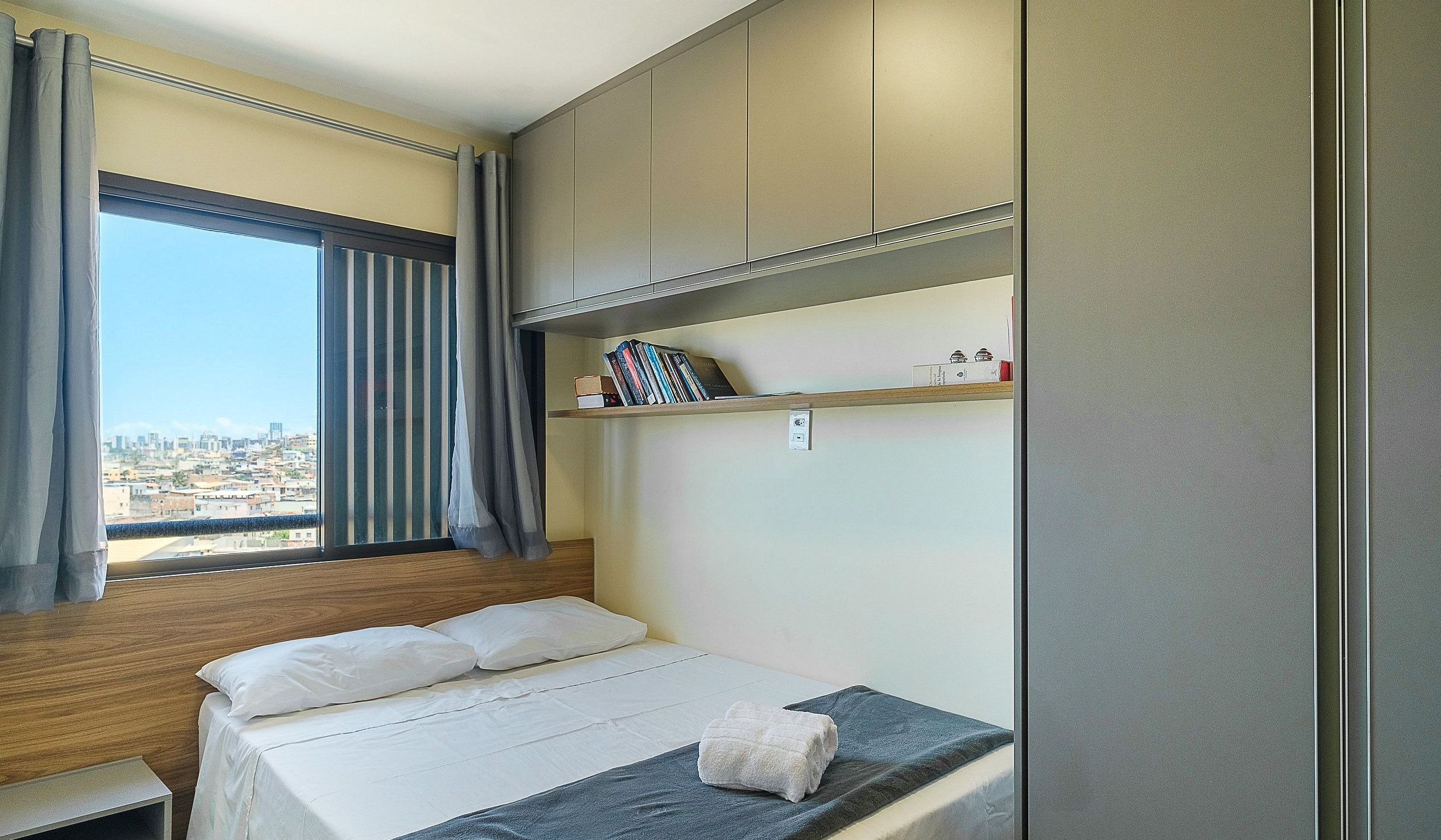Une chambre à coucher avec un lit, une fenêtre avec des rideaux, une vue sur la ville et des placards intégrés.