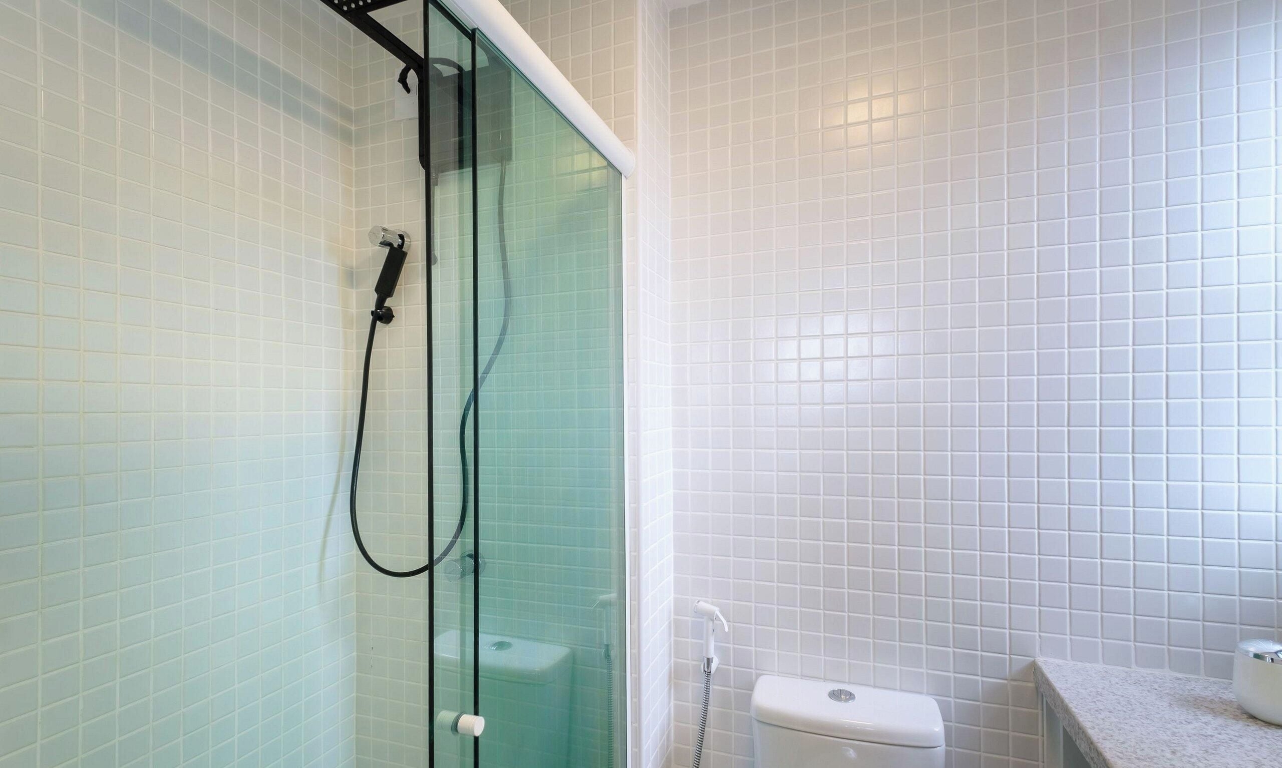 A bathroom with a glass-enclosed shower, white tiled walls, and a toilet.