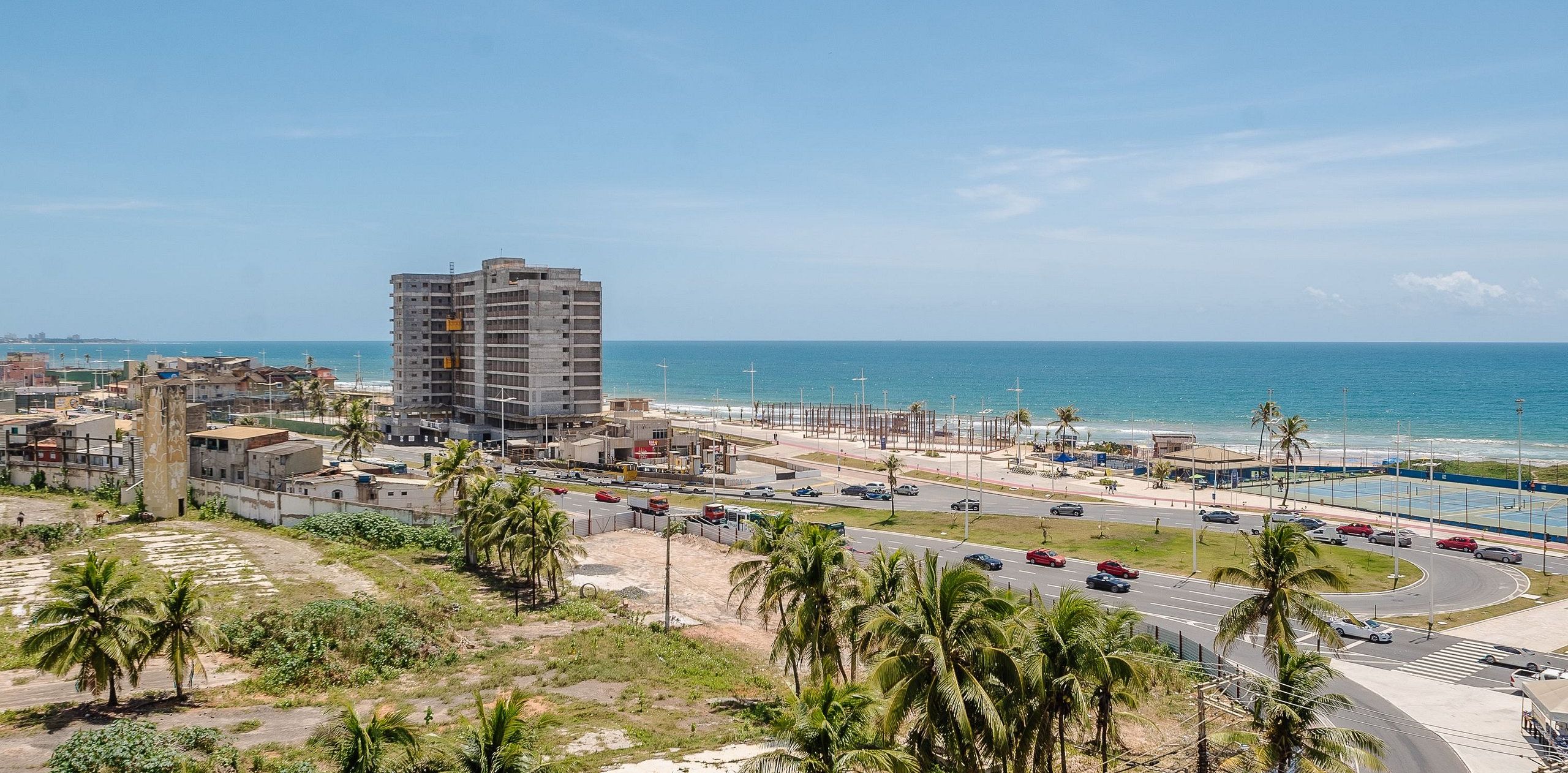 A coastal cityscape with a prominent multi-story building, a busy road with vehicles, and a beach in the background.