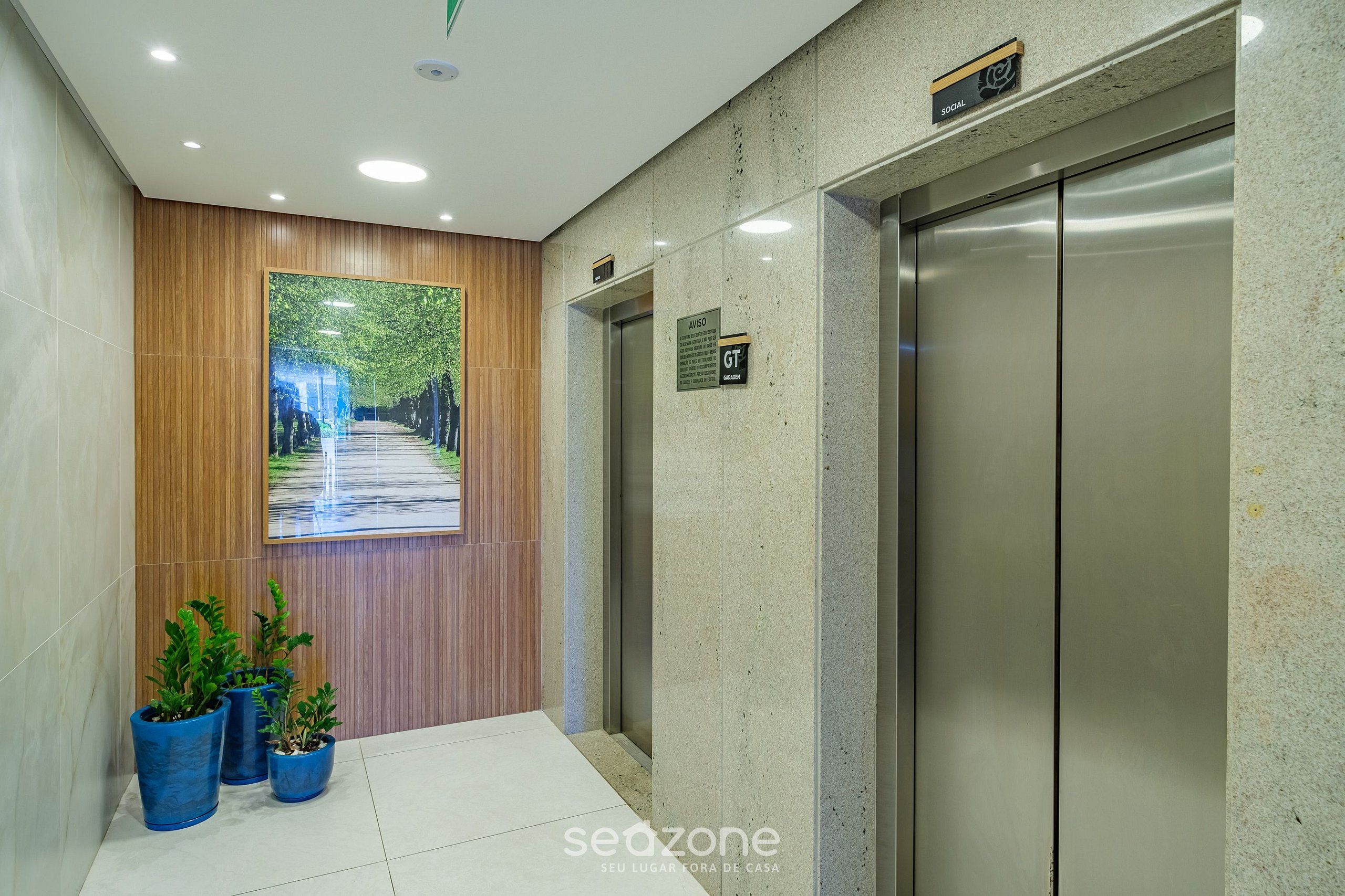 A modern elevator with a metallic finish, a wooden panel wall, and a digital display showing a tree-lined pathway.