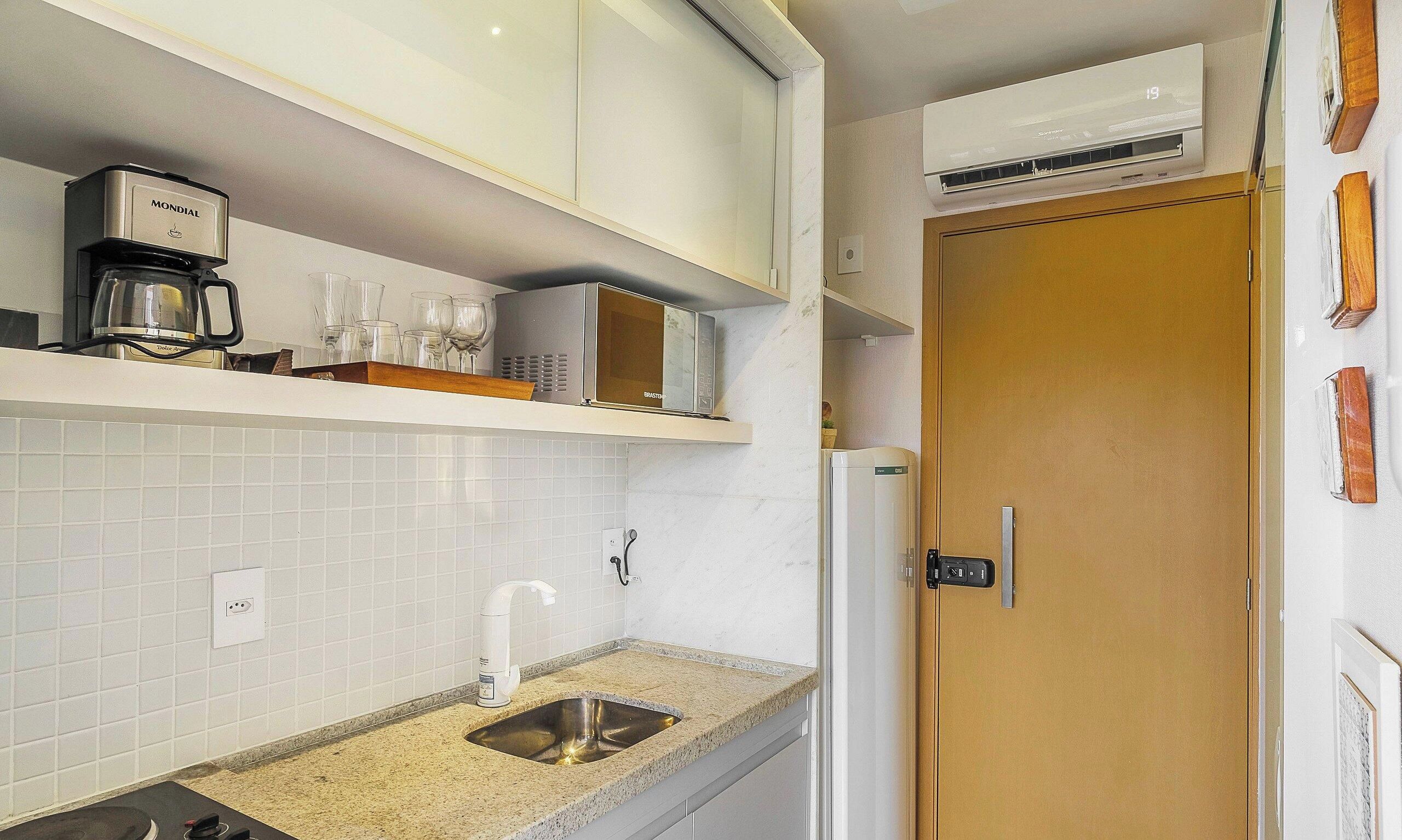 A compact kitchen with white cabinets, a built-in microwave, a coffee maker, and a sink with a faucet.