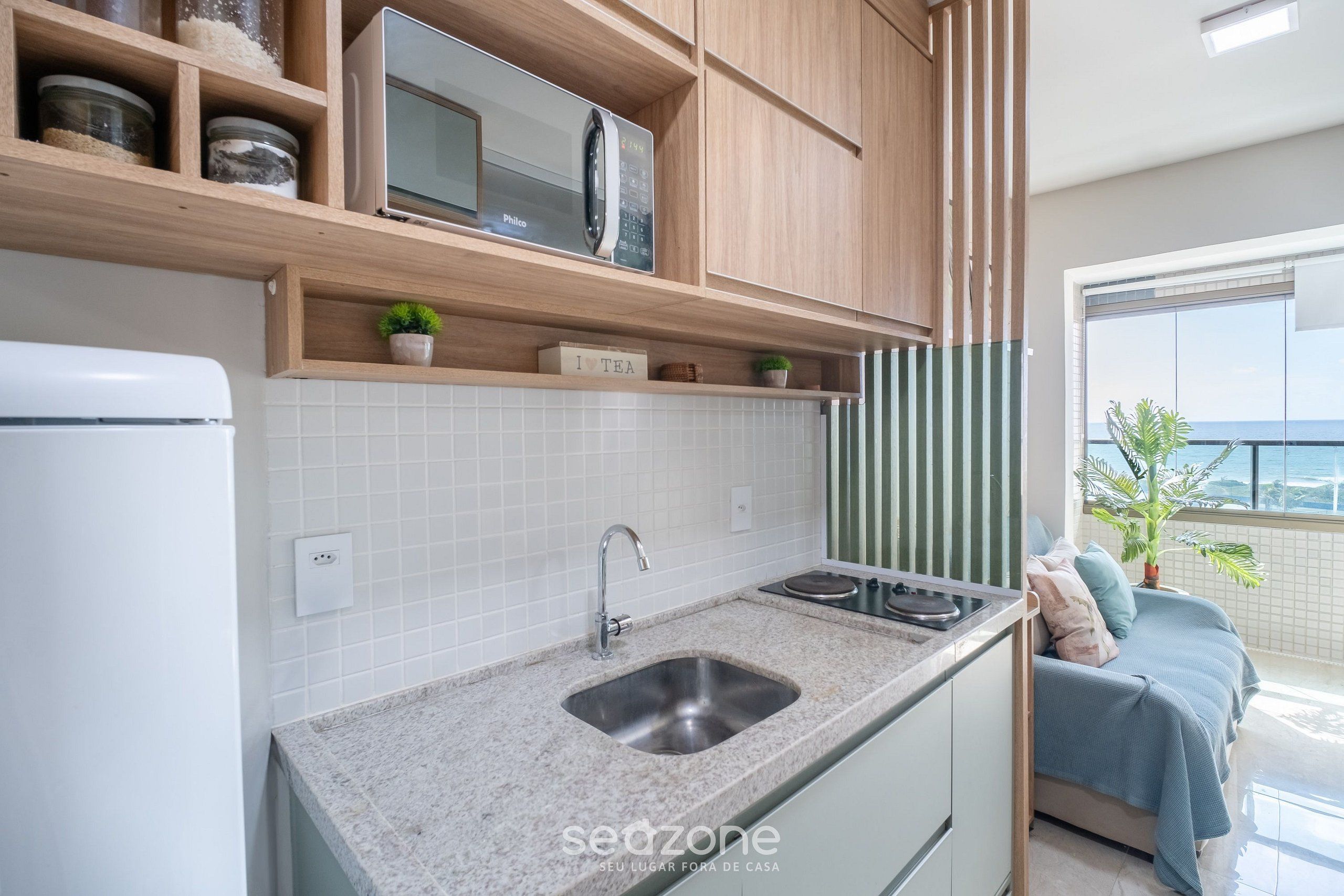 Una cocina moderna con microondas integrado, pileta de acero inoxidable y estantes de madera arriba.