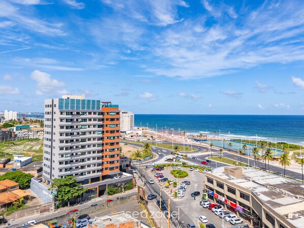 A high-rise hotel with multiple floors, a parking lot, and a view of the ocean.