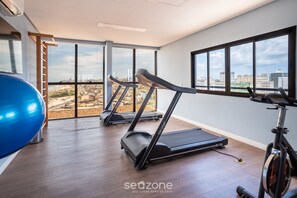 Un gimnasio con cintas de correr, una pelota de ejercicios azul y ventanas amplias con vistas a la ciudad.