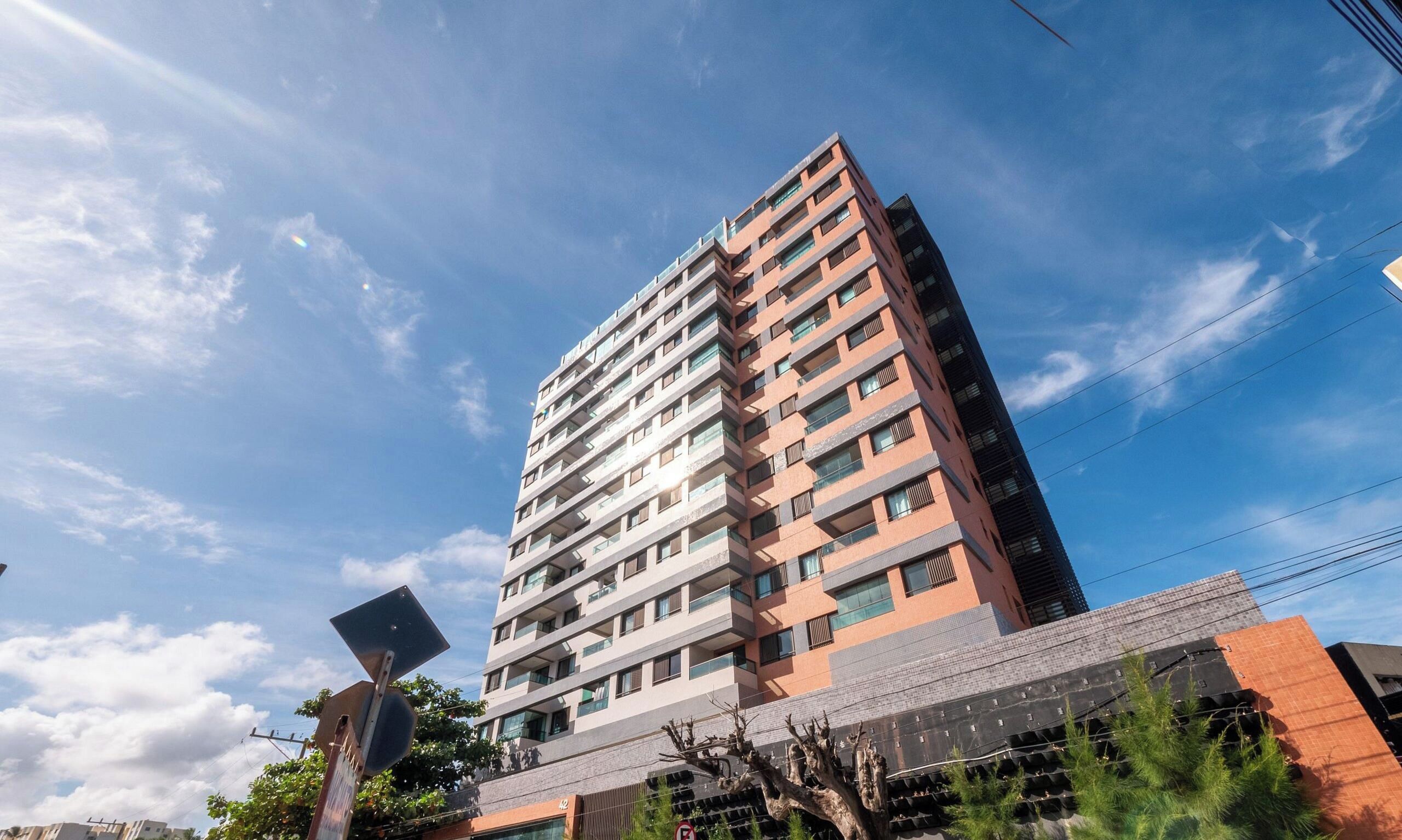 A multi-story residential building with a flat roof, multiple balconies, and a clear sky.