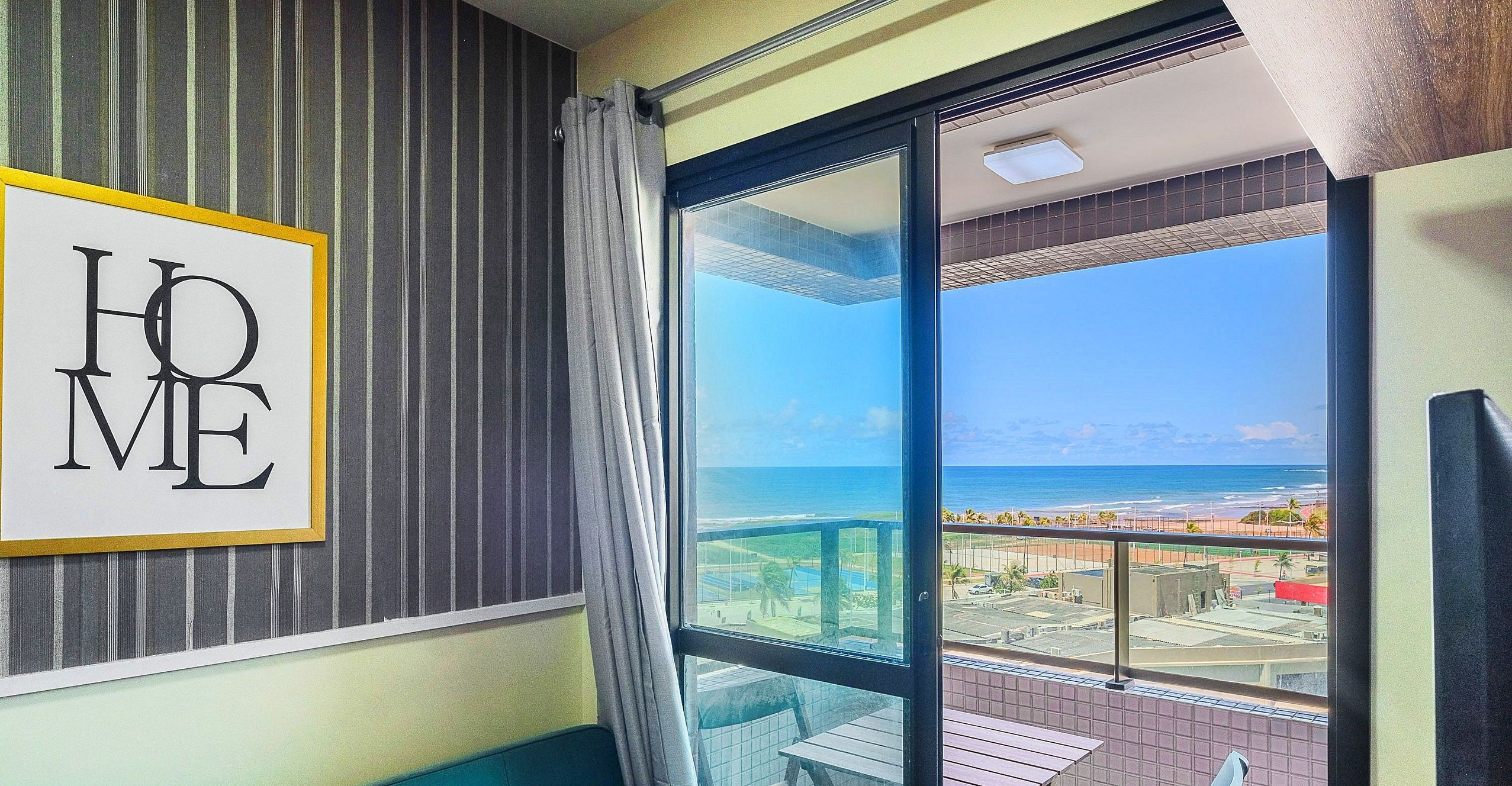 A room with a large window offering a view of the ocean and a cityscape.