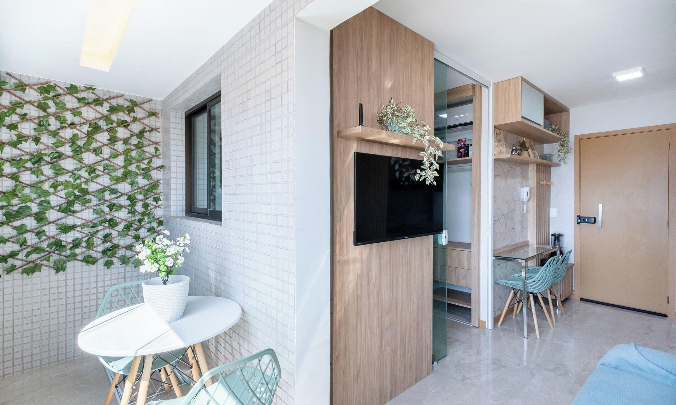 A modern interior with a tiled wall, a mounted TV, a dining area with chairs, and a wooden door.