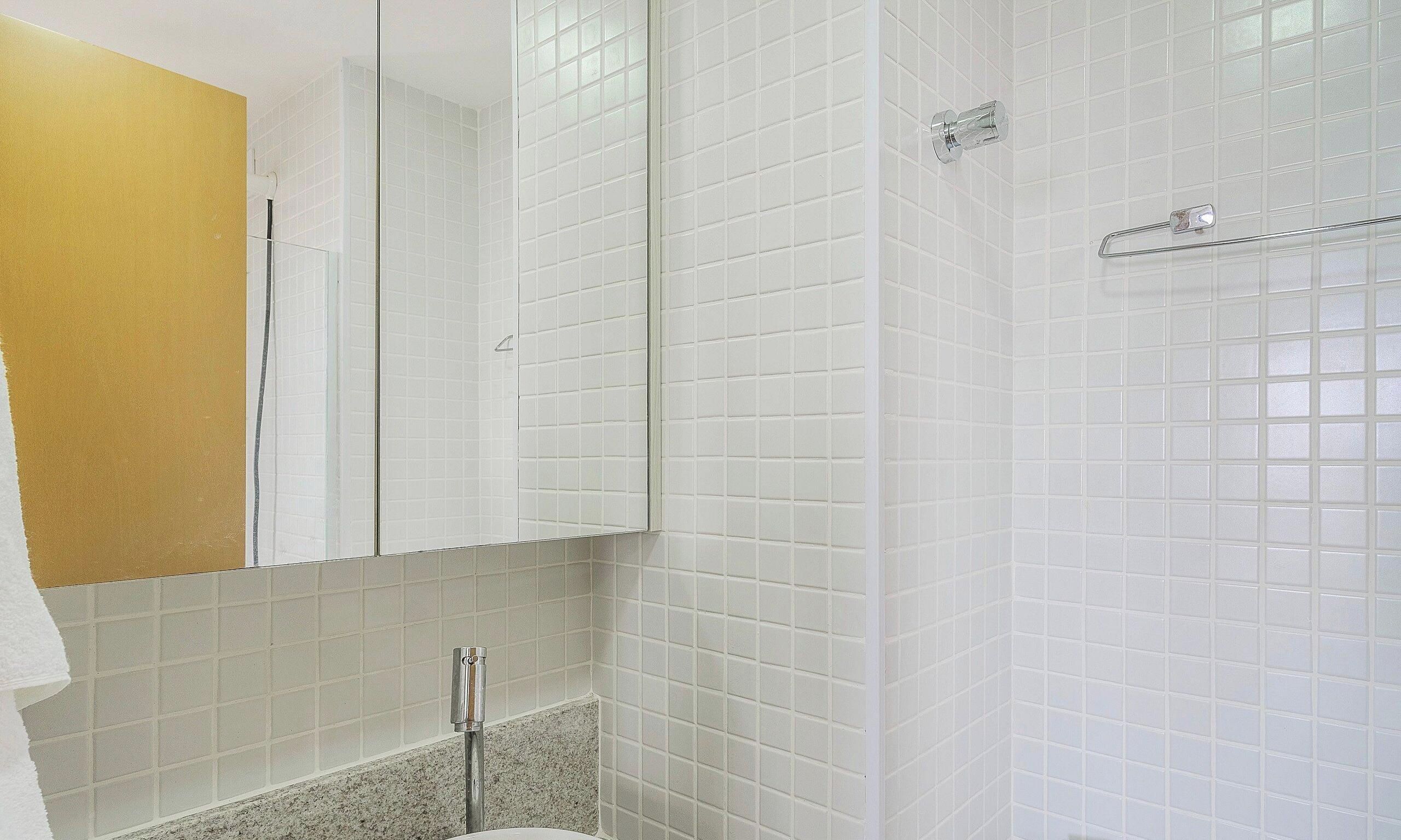 A bathroom with white tiled walls, a mirror, a towel, and a shower area.