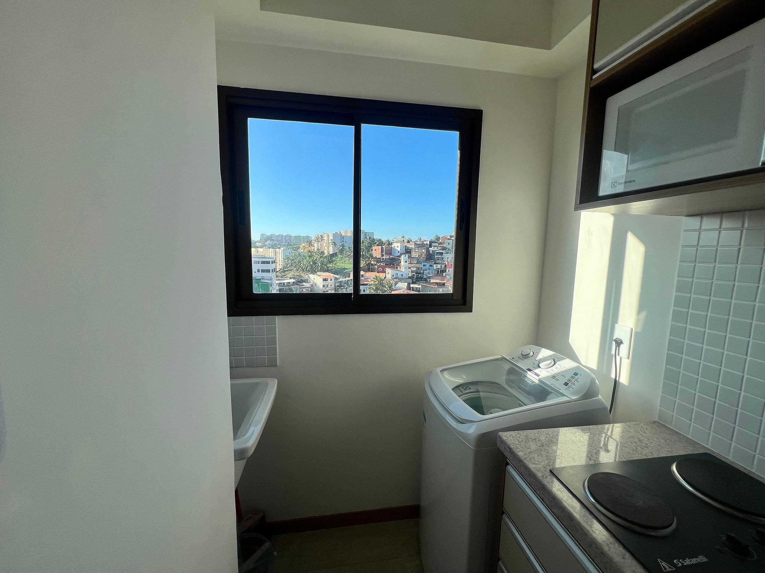 Cocina compacta con lavadora y secadora, ventana con vista a la ciudad y microondas sobre la encimera.