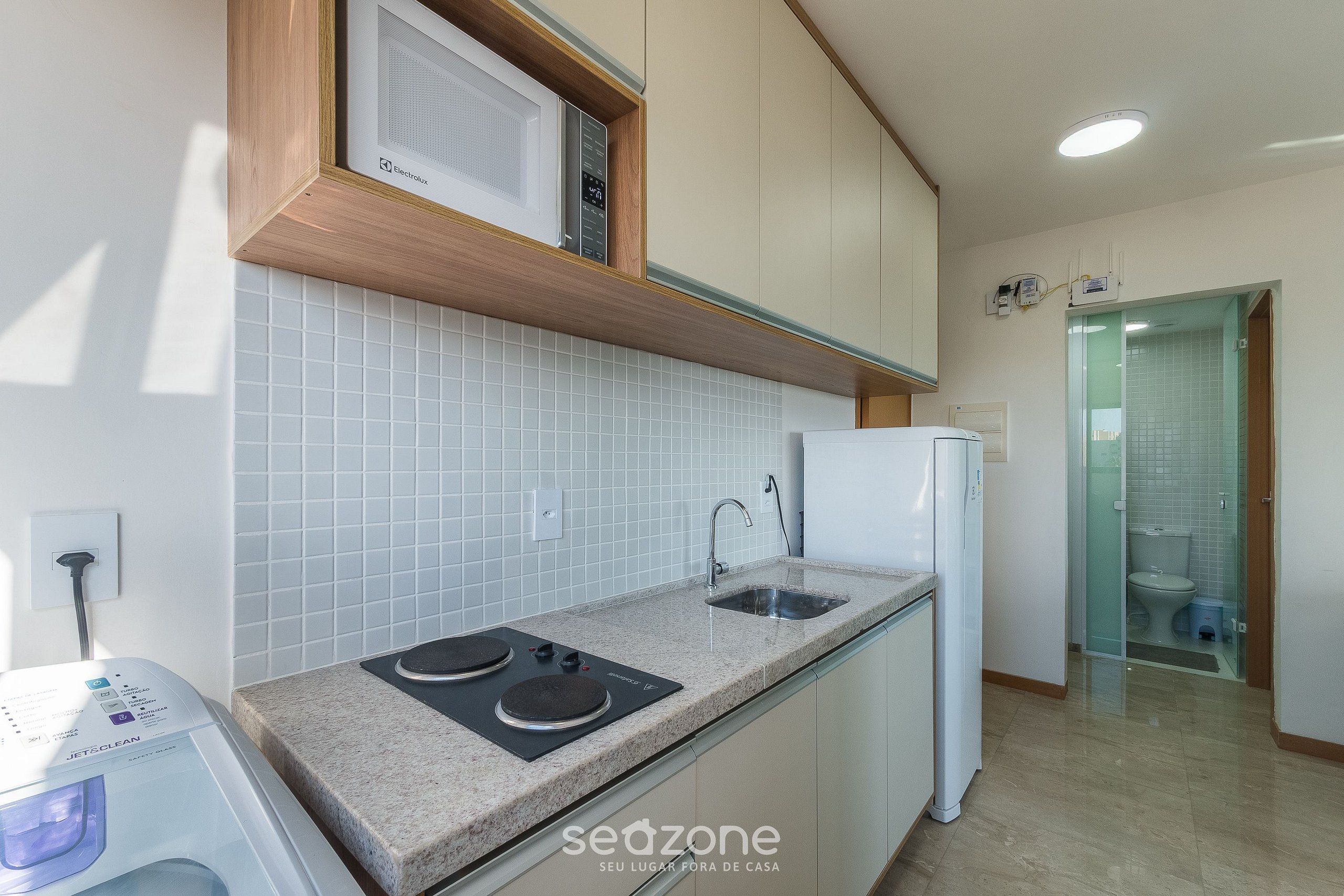 A modern kitchen with a built-in microwave, a sink, and a glass-enclosed shower area.