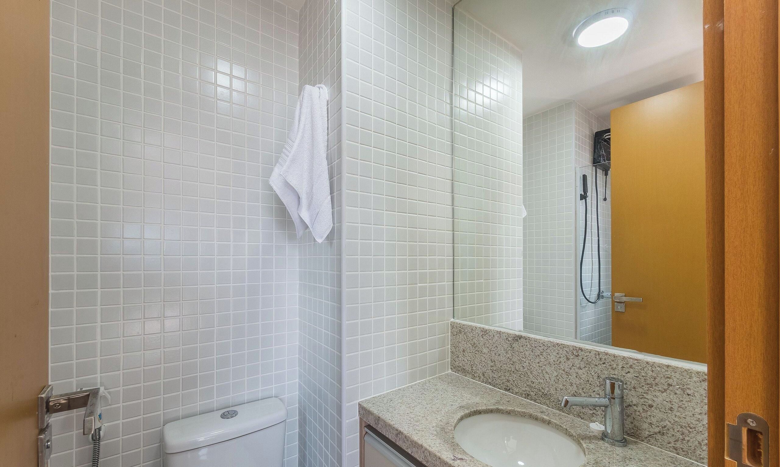 A bathroom with white tiled walls, a white toilet, a granite countertop sink, and a shower with a handheld showerhead.