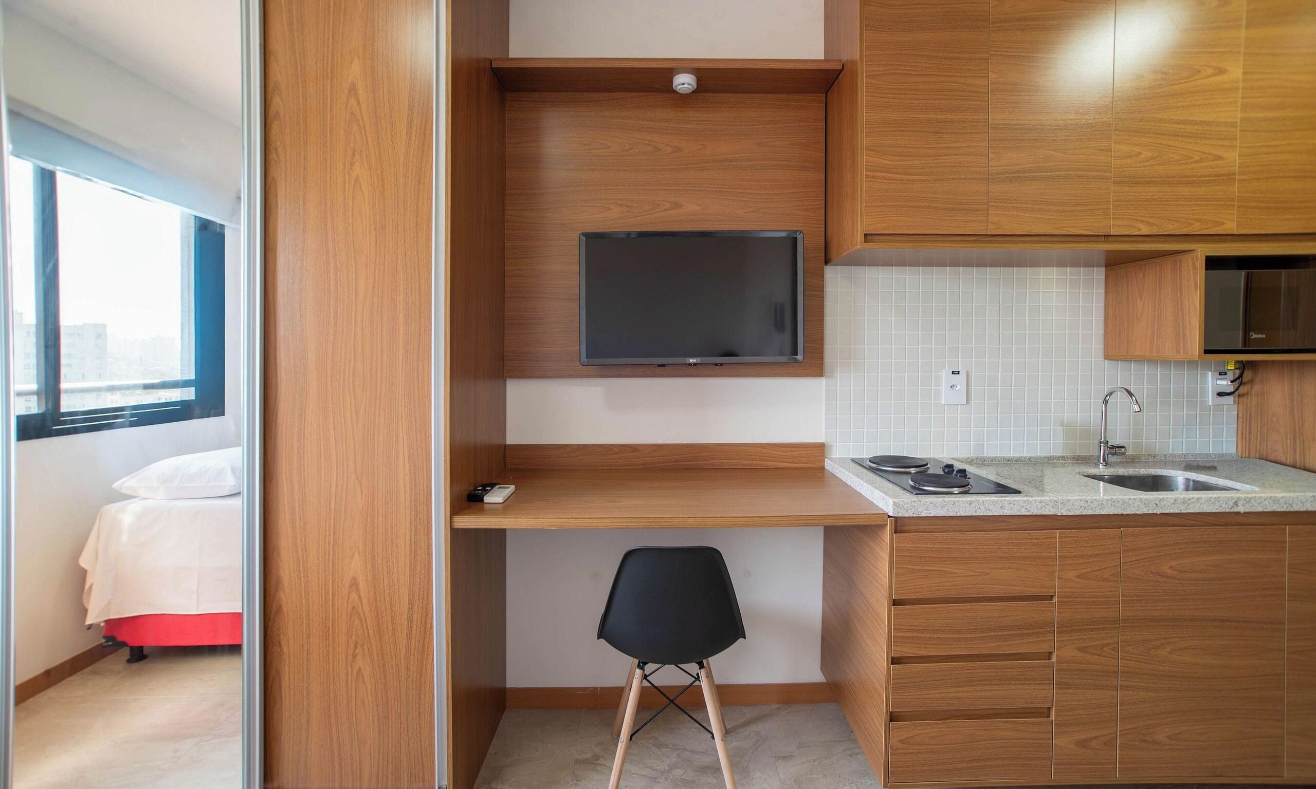 A compact kitchenette with a flat-screen TV, a small dining area, and a window with a view.