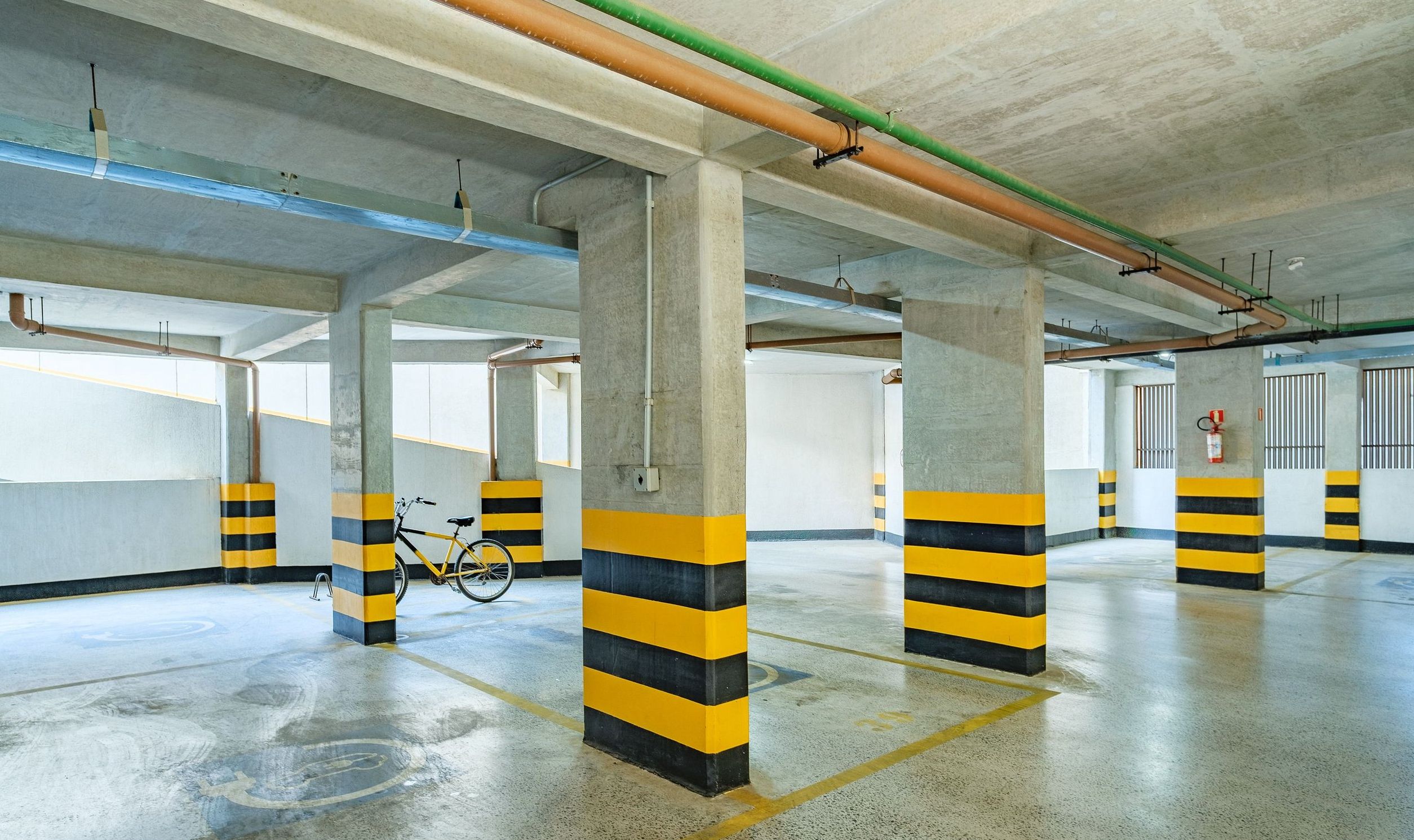 Un parking souterrain avec des piliers en béton, des barrières rayées de jaune et de noir, et un vélo garé.